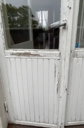 Altandörr med sliten vit färg kring glas och panel, före renovering.