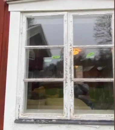 Vitmålat spröjsfönster med sliten yta på röd träfasad, före renovering.