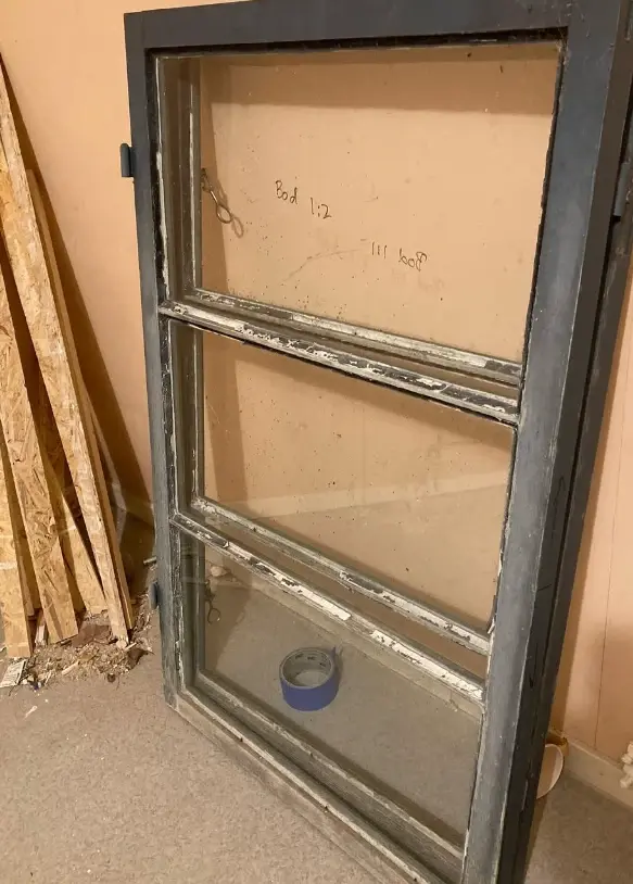 Sliten fönsterbåge med tre rutor i verkstad före renovering.