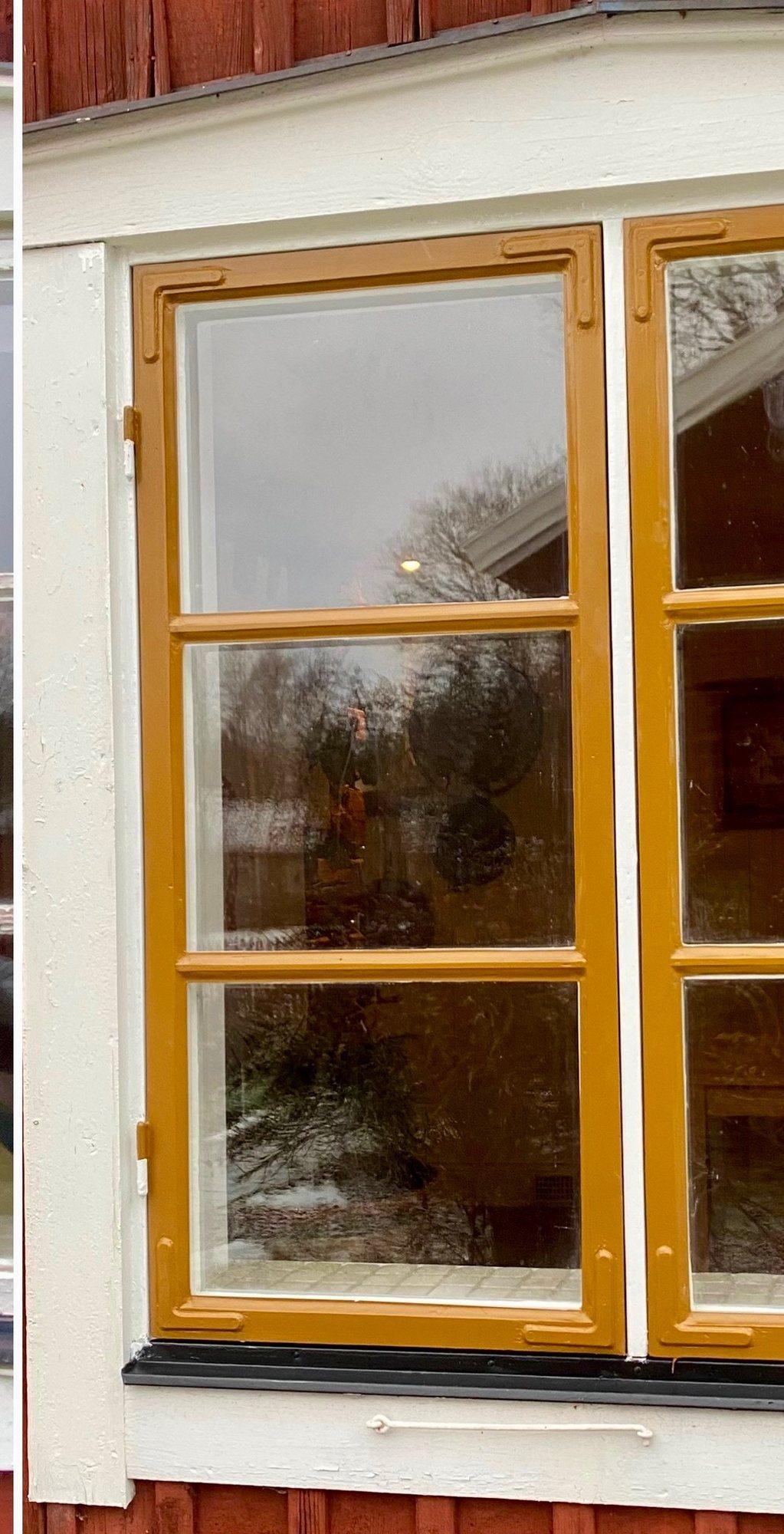 Renoverat spröjsat träfönster målat i varm ockra på röd träfasad.