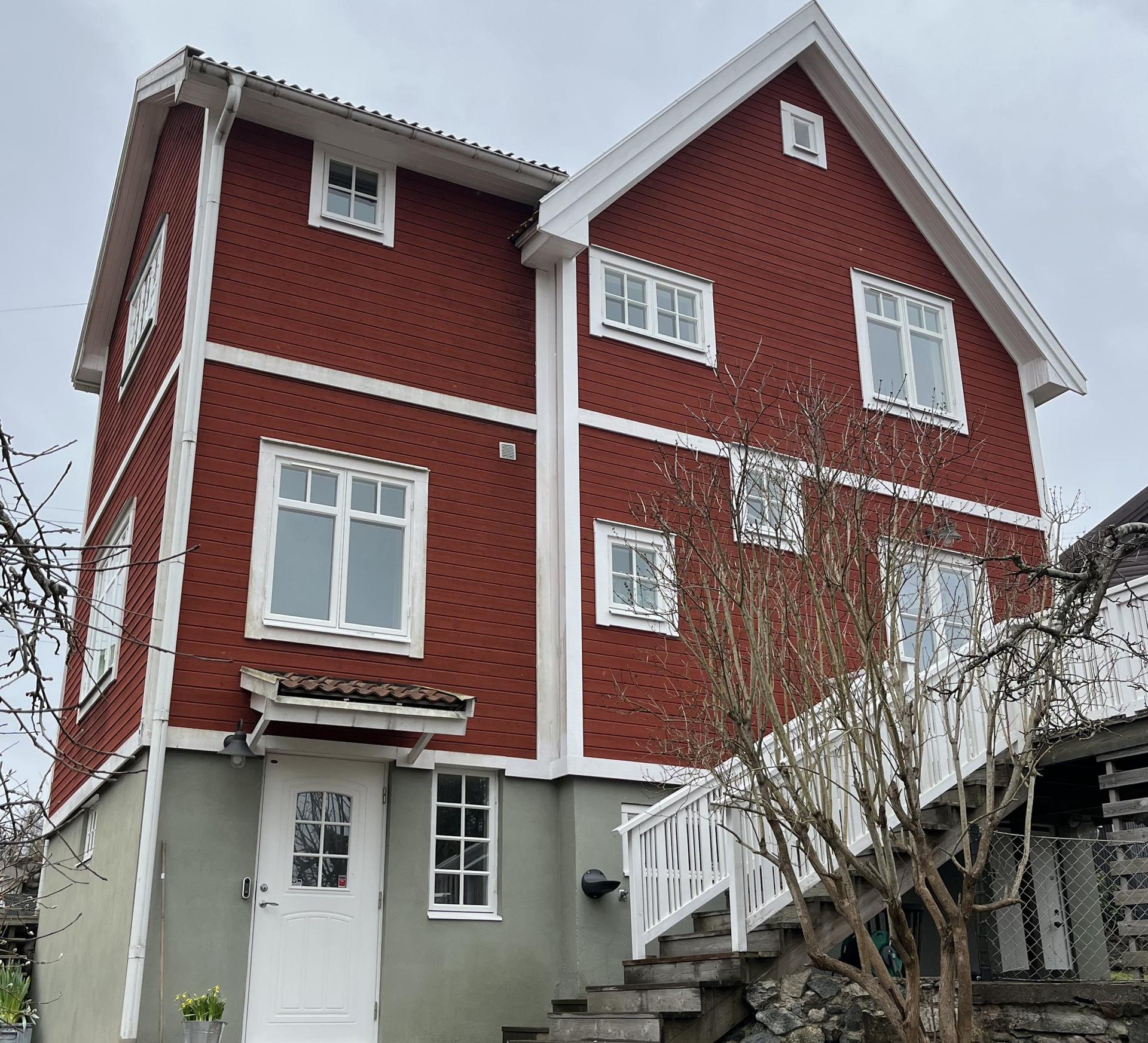 Falurött trähus i tre plan med vitmålade träfönster och vita knutar.
